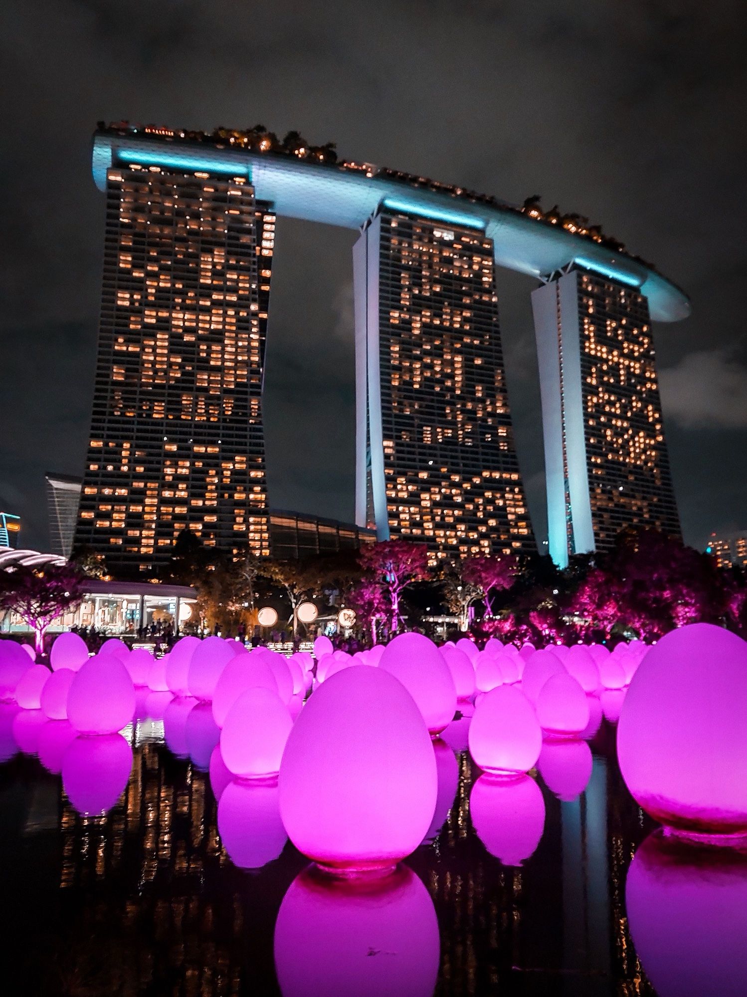 Glowing pink egg-shaped lights on the water below Marina Bay Sands